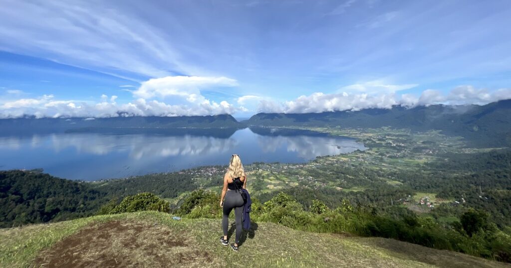 Blonde girl stands on the ridge over Maninjau Lake.