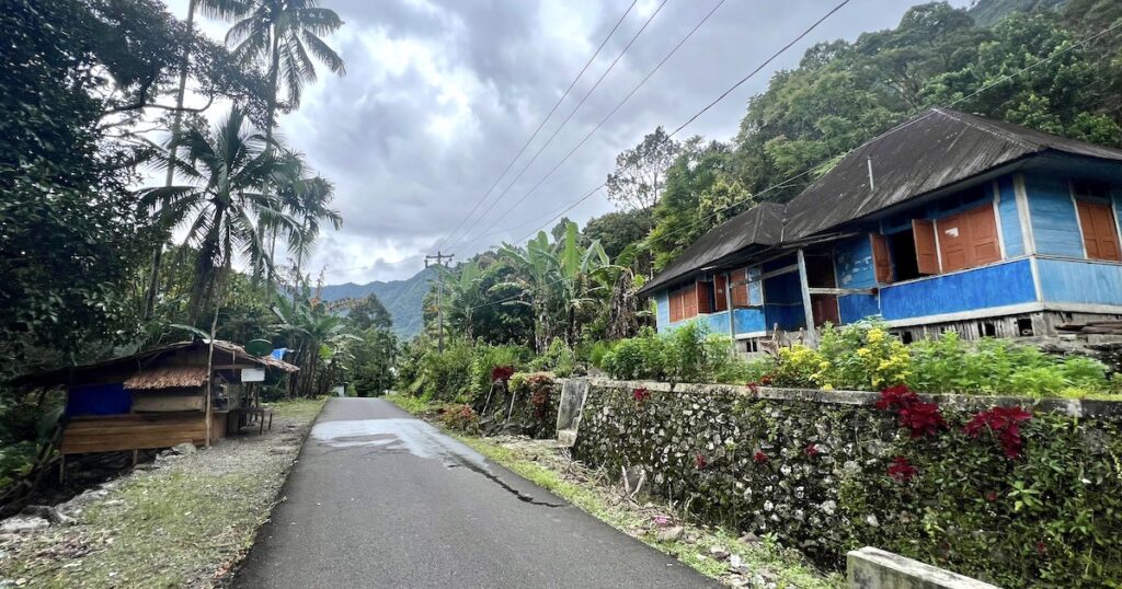 A tarmac road runs between thatched houses on the west shore of Lake Maninjau.