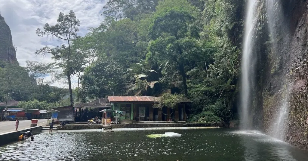 The Harau Valley waterfall water pool with locals bathing and an adjacent street.