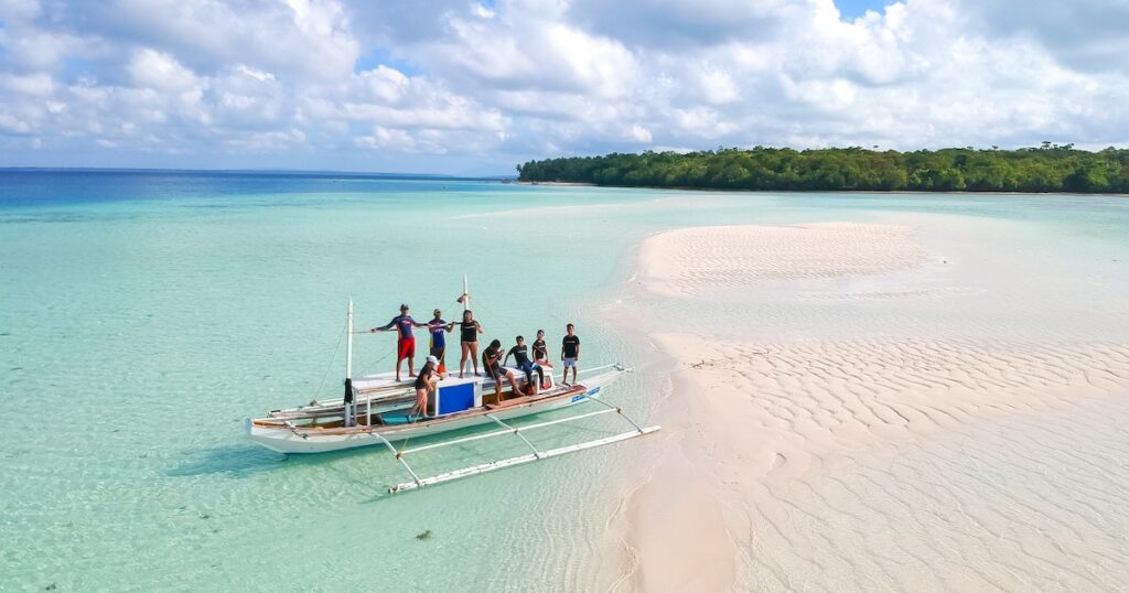 Crew stand on a bangka boat on a pink sand island in Balabac Palawan.