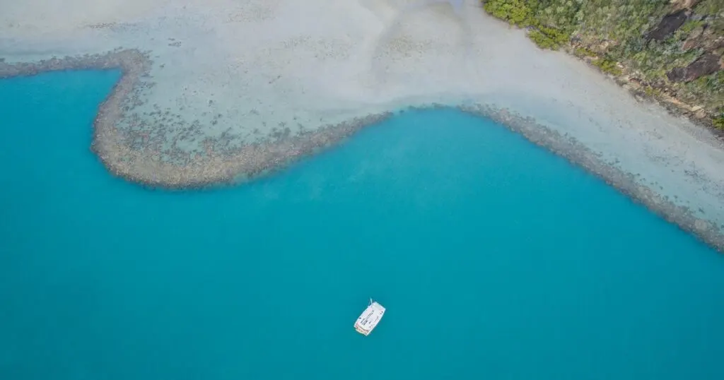 Aerial view of a lone white sailing boat floats just off shore in the Whitsundays.