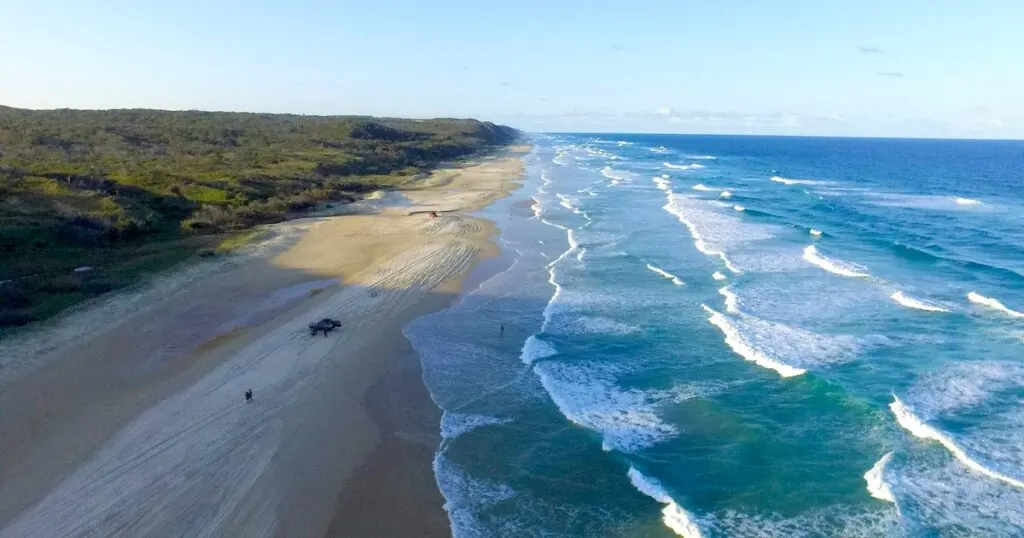 Aerial view of 75 Mile Beach in K'Gari, with jeeps dotted along the sand.