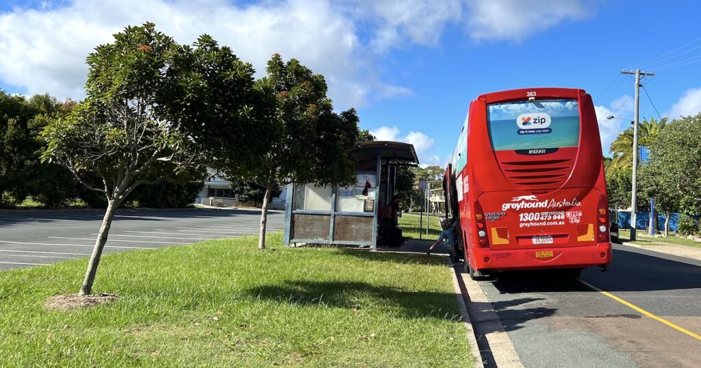 A red Greyhound bus parked at a bus stop on the side of the road in Queensland.