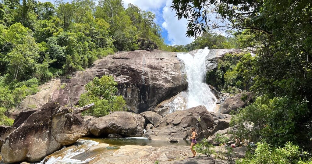 A woman walks in front of the Josephine Falls waterfall Wooroonooran on a Cairns to Mission Beach road trip.