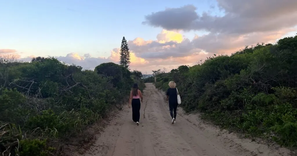 Two women walk down a dirt trick towards 75 Mile Beach on Fraser Island.