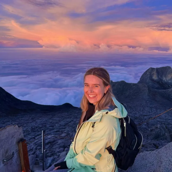 Escape Artist Katie blogger Katie Treharne sits at the top of Mount Kinabalu in Borneo at sunset.