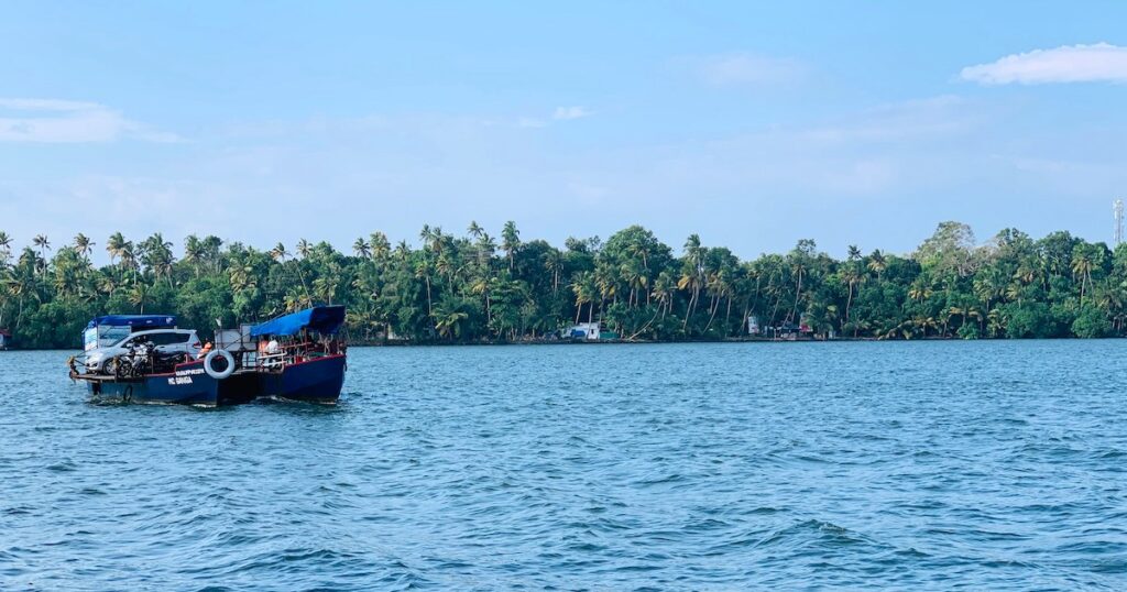 A boat glides along the Kollam backwaters, surrounded by palm trees.