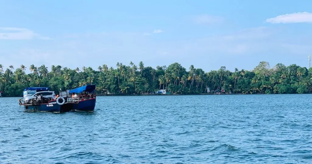 A boat glides along the Kollam backwaters, surrounded by palm trees.