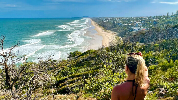 Woman with a blonde ponytail looks out over Sunshine Beach from Noosa National park.