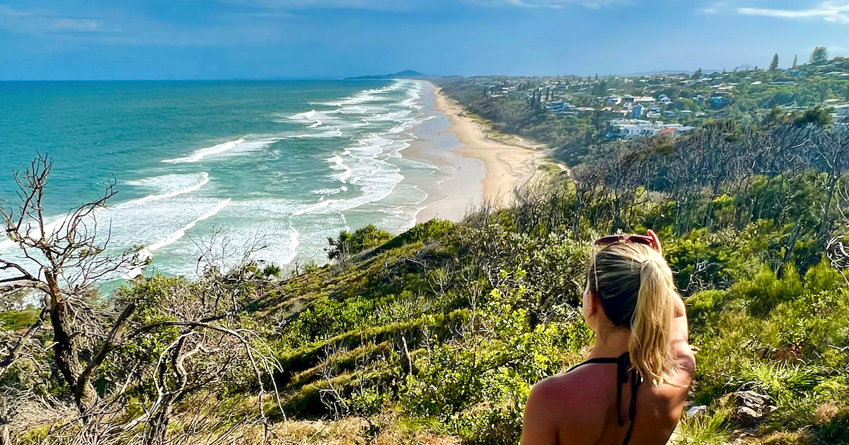 Woman with a blonde ponytail looks out over Sunshine Beach from Noosa National park.