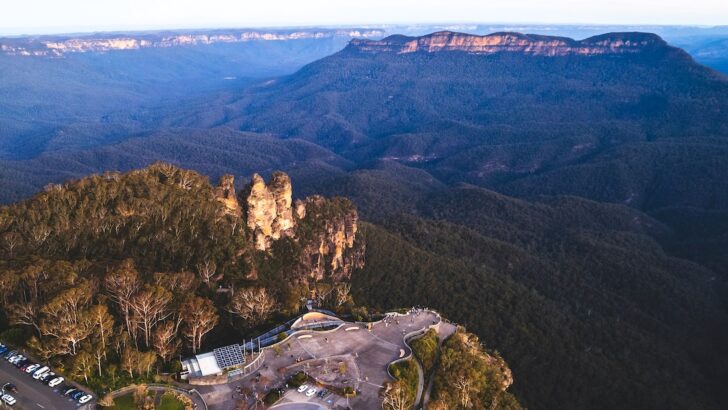 Aerial view of three sandstone peaks next to the Jamison Valley and a tarmac viewpoint.