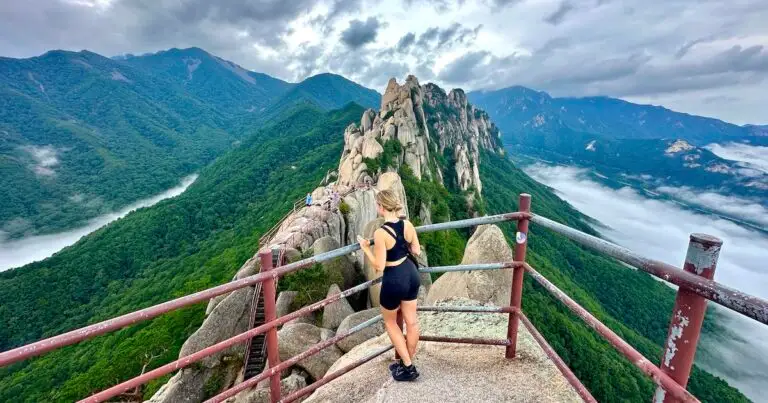 Woman wearing hiking gear gazes over Ulsanbawi's granite boulders and a green valley.
