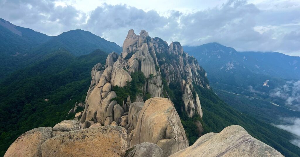 Granite boulders tower over green forested slopes and clouds at Ulsanbawi mountain in Seoraskan National Park.