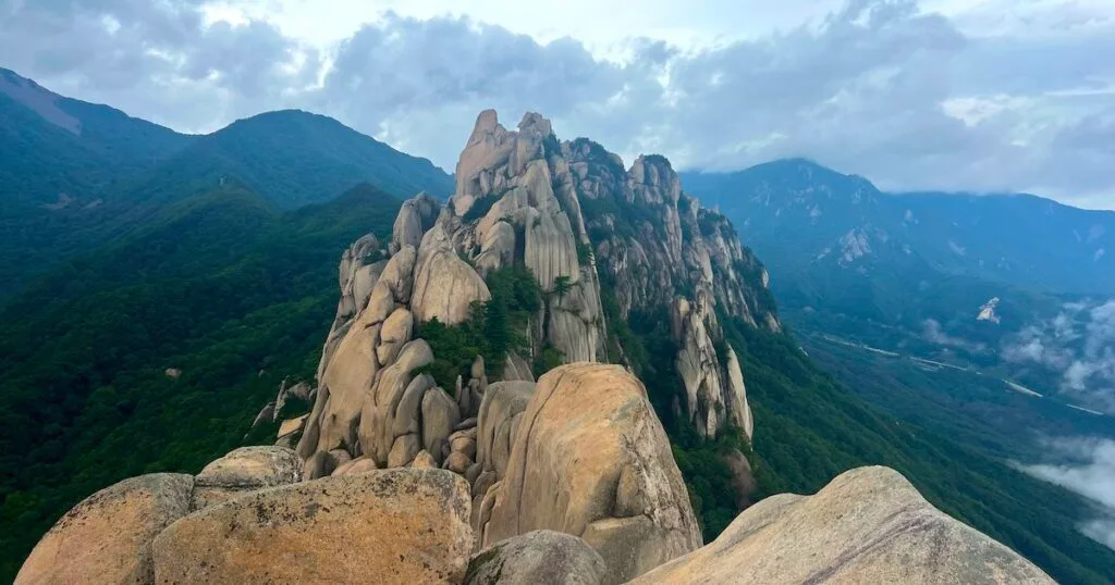 Granite boulders tower over green forested slopes and clouds at Ulsanbawi mountain in Seoraskan National Park.