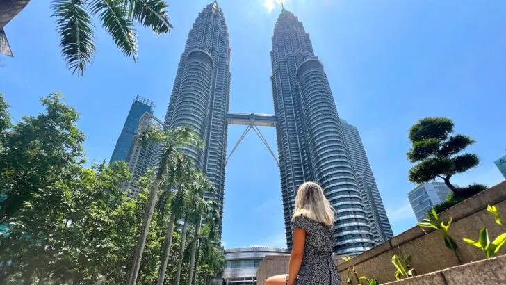 Woman sits at the bottom of the Petronas Towers, one of the best places to visit on a Kuala Lumpur itinerary.