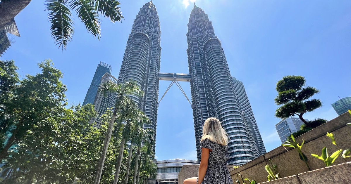 Woman sits at the bottom of the Petronas Towers, one of the best places to visit on a Kuala Lumpur itinerary.