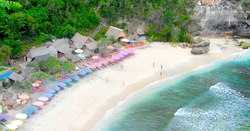 View down over sunbeds and huts along the sandy Atuh Beach in Nusa Penida.