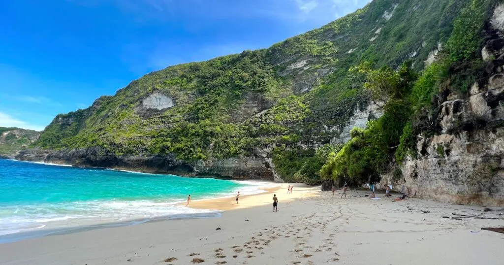 Footprints in the sand at Kelingking Beach, surrounded by high, green cliffs.