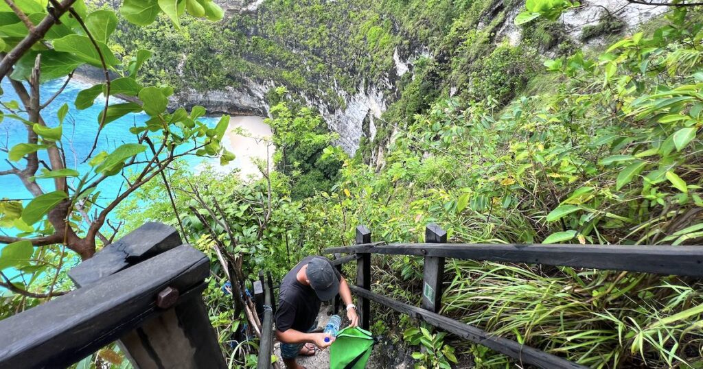 A person rests on the steep hike down to Kelingking Beach, with railings on either side.