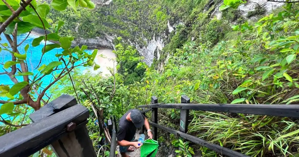 A person rests on the steep hike down to Kelingking Beach, with railings on either side.