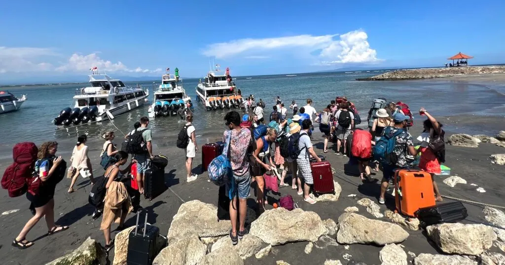 A group of passengers wade through shallow seawater to reach fast boats at Sanur Port.
