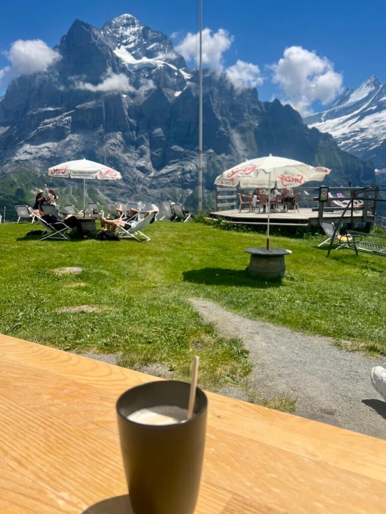 Outdoor cafรฉ terrace with deck chairs overlooking dramatic snow-capped Alpine mountains.