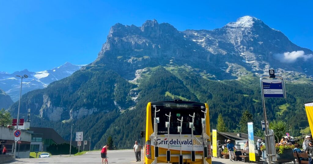 Yellow Grindelwald bus waiting at a bus stop with towering Alpine peaks rising behind the village.
