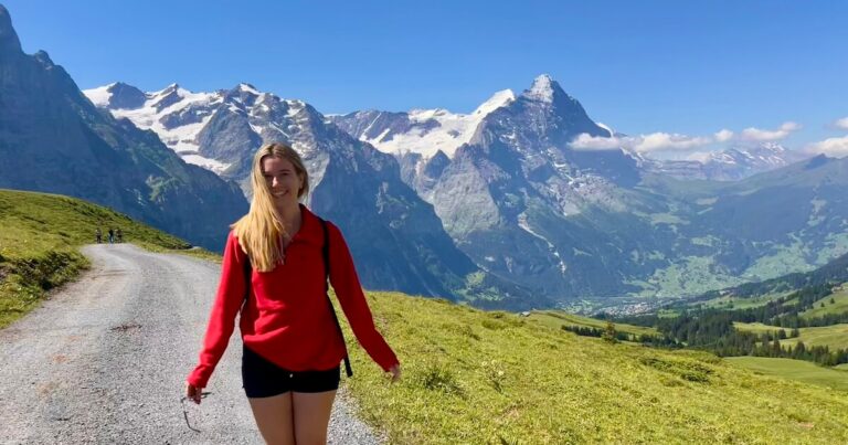 Rolling green Alpine hills dotted with mountain chalets beneath dramatic clouds and rugged peaks.